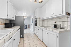 Kitchen with black electric stovetop, tile counters, and white cabinets