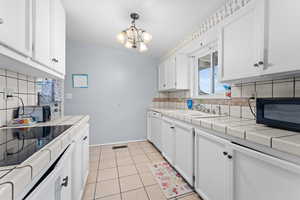 Kitchen with sink, dishwasher, white cabinetry, hanging light fixtures, and tile countertops