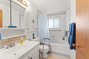 Full bathroom featuring decorative backsplash, tile patterned flooring, vanity, shower / tub combo, and toilet