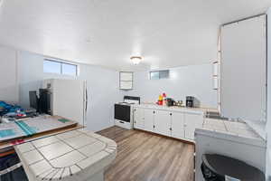 Kitchen with white appliances, light hardwood / wood-style flooring, white cabinetry, a textured ceiling, and tile countertops