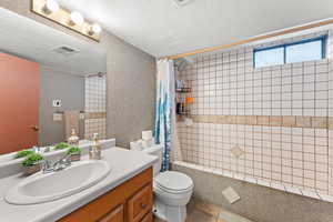 Full bathroom with shower with curtain, vanity, toilet, tile patterned floors, and a textured ceiling