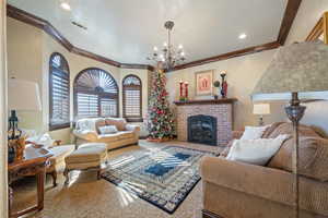 Carpeted living room featuring a brick fireplace, crown molding, and a notable chandelier