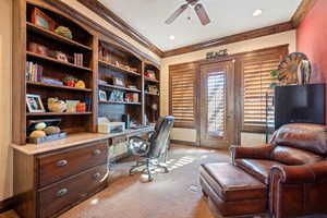 Carpeted office space with crown molding, ceiling fan, and built in desk