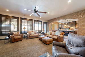 Carpeted living room with ceiling fan with notable chandelier, a textured ceiling, and brick wall