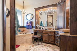 Bathroom with an inviting chandelier, vanity, and tiled bath