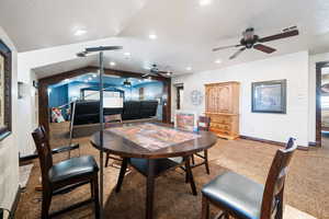 Dining space with vaulted ceiling, light colored carpet, ceiling fan, and a textured ceiling