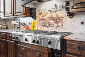 Kitchen featuring stainless steel gas stovetop, dark brown cabinets, light stone counters, and decorative backsplash