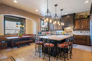 Kitchen featuring a breakfast bar, dark brown cabinetry, light stone countertops, a center island with sink, and breakfast area