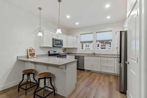 Kitchen with stainless steel appliances, decorative light fixtures, kitchen peninsula, and white cabinets