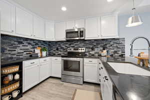 Kitchen with appliances with stainless steel finishes, sink, pendant lighting, and white cabinets