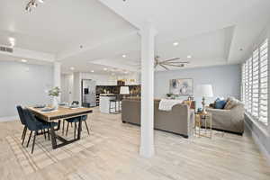 Dining room with ceiling fan, a raised ceiling, decorative columns, and light wood-type flooring