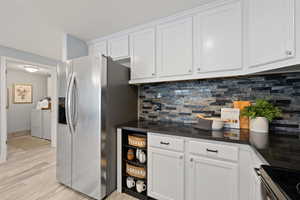 Kitchen featuring white cabinetry, separate washer and dryer, stainless steel appliances, light hardwood / wood-style floors, and backsplash