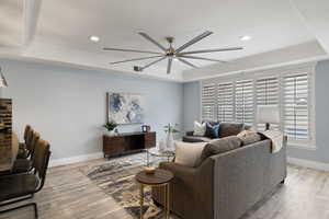 Living room featuring ceiling fan, ornamental molding, light hardwood / wood-style floors, and a tray ceiling