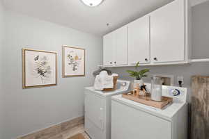 Washroom featuring light hardwood / wood-style flooring, cabinets, and washing machine and clothes dryer