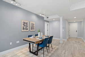 Dining room featuring ornate columns, rail lighting, and light wood-type flooring