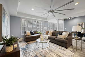 Living room featuring rail lighting, light hardwood / wood-style floors, a raised ceiling, and ornate columns