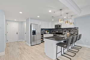 Kitchen featuring appliances with stainless steel finishes, decorative light fixtures, white cabinets, a kitchen bar, and kitchen peninsula