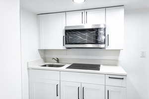 Kitchen with black electric stovetop, sink, and white cabinets