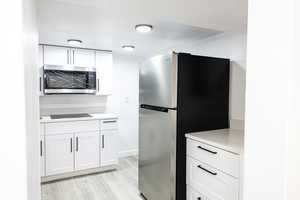 Kitchen with appliances with stainless steel finishes, white cabinets, and light hardwood / wood-style floors