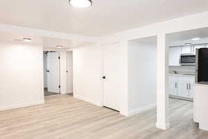 Basement with stainless steel fridge and light wood-type flooring