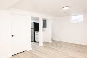 Basement with stainless steel refrigerator, electric panel, and light hardwood / wood-style floors