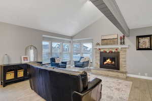 Living room featuring a stone fireplace, plenty of natural light, high vaulted ceiling, and light wood-type flooring