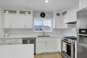 Kitchen featuring white cabinetry, sink, decorative backsplash, stainless steel appliances, and light stone countertops