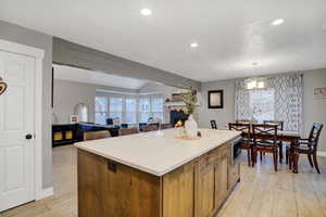 Kitchen featuring a kitchen island, stainless steel microwave, decorative light fixtures, a textured ceiling, and light hardwood / wood-style flooring