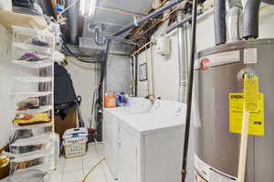 Clothes washing area featuring light tile patterned floors, washer and dryer, and gas water heater