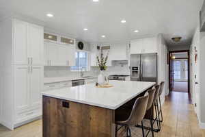 Kitchen featuring white cabinetry, light stone counters, a kitchen breakfast bar, a kitchen island, and stainless steel appliances