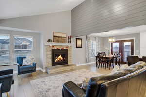 Living room featuring a stone fireplace, high vaulted ceiling, and light hardwood / wood-style floors