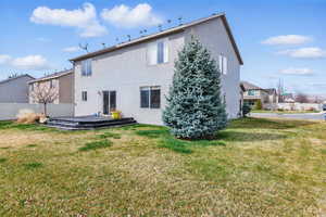 Rear view of property with stucco siding, a deck, fence, and a yard