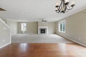 Unfurnished living room featuring crown molding, a healthy amount of sunlight, ceiling fan with notable chandelier, and wood finished floors
