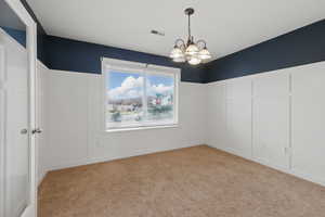 Carpeted empty room with a decorative wall, visible vents, a chandelier, and wainscoting