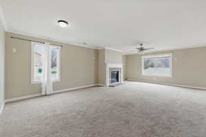 Unfurnished living room with a fireplace, ceiling fan, carpet, and crown molding