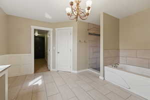 Bathroom with an inviting chandelier, a tile shower, and a bath