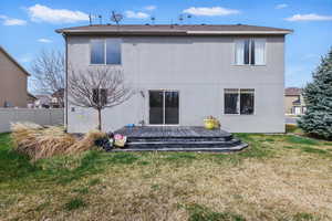 Rear view of property featuring stucco siding, fence, a wooden deck, and a yard