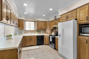 Solid wood cabnets, sink, crown molding, decorative backsplash, and appliances with stainless steel finishes