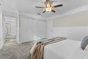 Master bedroom featuring crown molding, ceiling fan, connected bathroom, and two closets