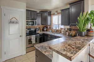 Kitchen with stainless steel appliances, light tile patterned flooring, sink, and kitchen peninsula