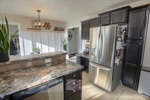 Kitchen with appliances with stainless steel finishes, pendant lighting, a notable chandelier, and light tile patterned floors