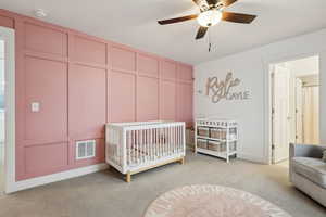 Carpeted bedroom featuring a nursery area and ceiling fan