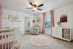 Carpeted bedroom featuring a crib and ceiling fan