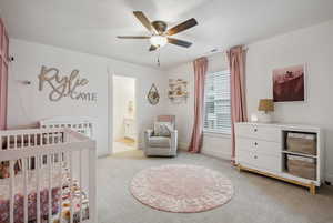 Bedroom featuring ceiling fan, light carpet, and a crib