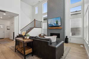 Living room with a wealth of natural light, light hardwood / wood-style floors, a large fireplace, and a high ceiling