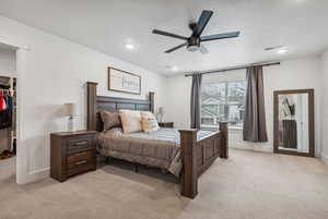 Carpeted bedroom with ceiling fan, a walk in closet, a closet, and a textured ceiling