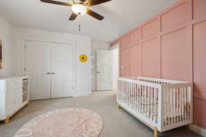 Carpeted bedroom with a crib, ceiling fan, and a closet