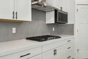 Kitchen with ventilation hood, tasteful backsplash, appliances with stainless steel finishes, and white cabinets