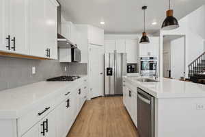 Kitchen featuring stainless steel appliances, an island with sink, white cabinetry, and decorative light fixtures