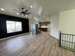 Unfurnished living room with vaulted ceiling, ceiling fan, and light wood-type flooring